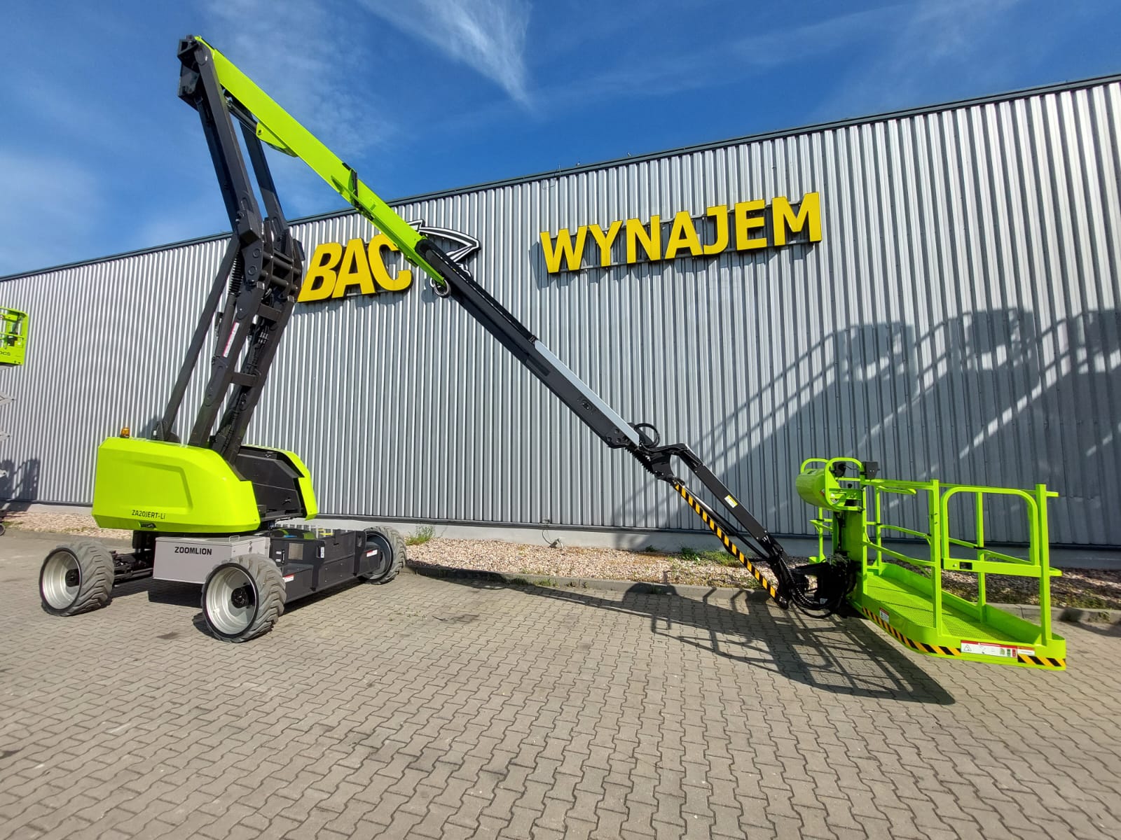 Podnośnik koszowy Zoomlion przed budynkiem z napisem "Wynajem".