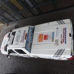 Samochód rajdowy z reklamami na parkingu.