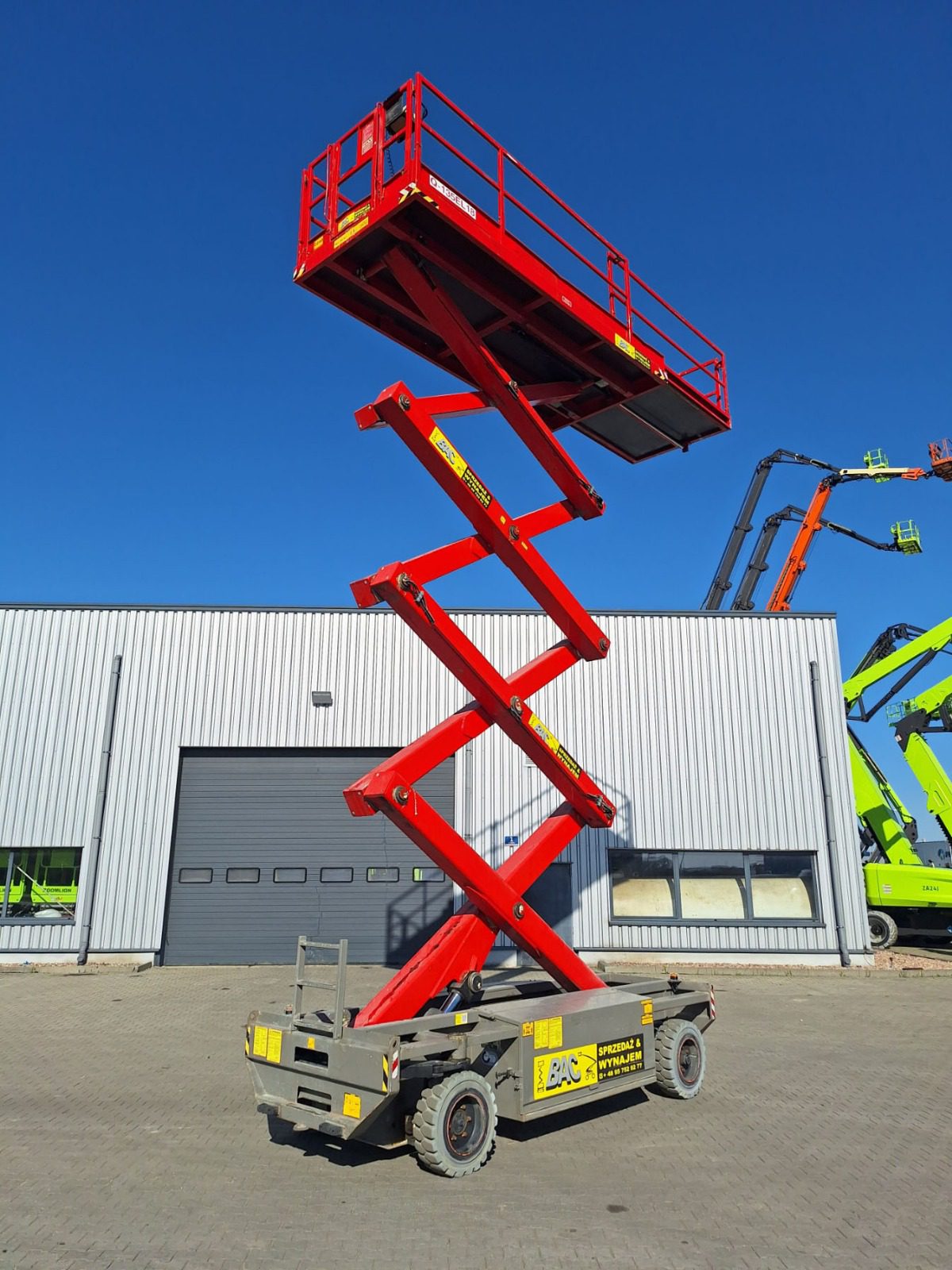 Podnośnik nożycowy Holland Lift Q135EL18 podczas pracy na wysokości – elektryczny model o maksymalnym zasięgu 13,5 metra, idealny do zastosowań wewnętrznych i zewnętrznych, wynajem w Bac Polska.