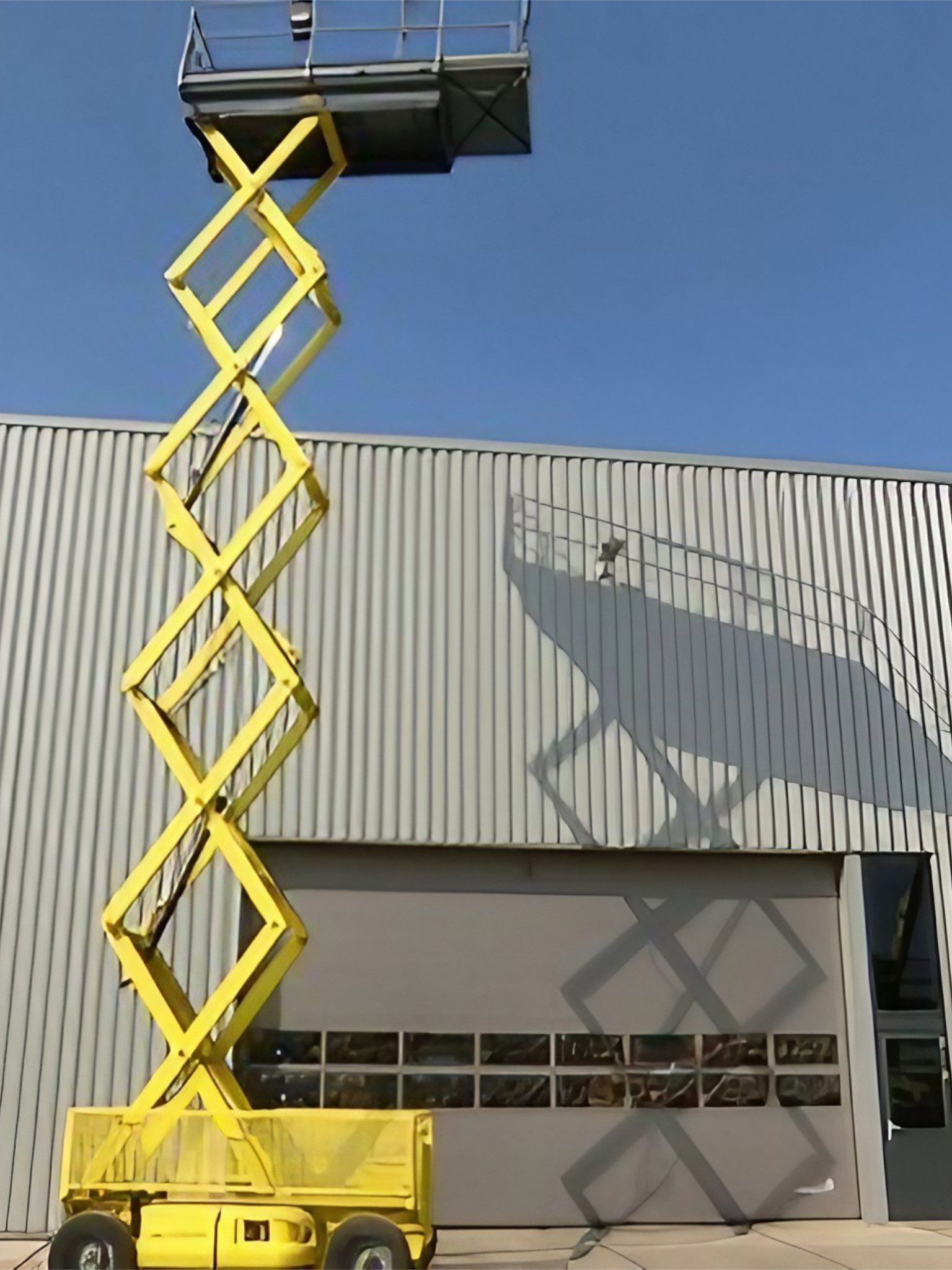 Gelbe Scherenbühne vor einem Industriegebäude.