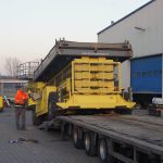 Załadunek sprzętu budowlanego na przyczepę ciężarową.