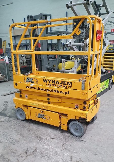 Podnośnik nożycowy żółty na hali przemysłowej.