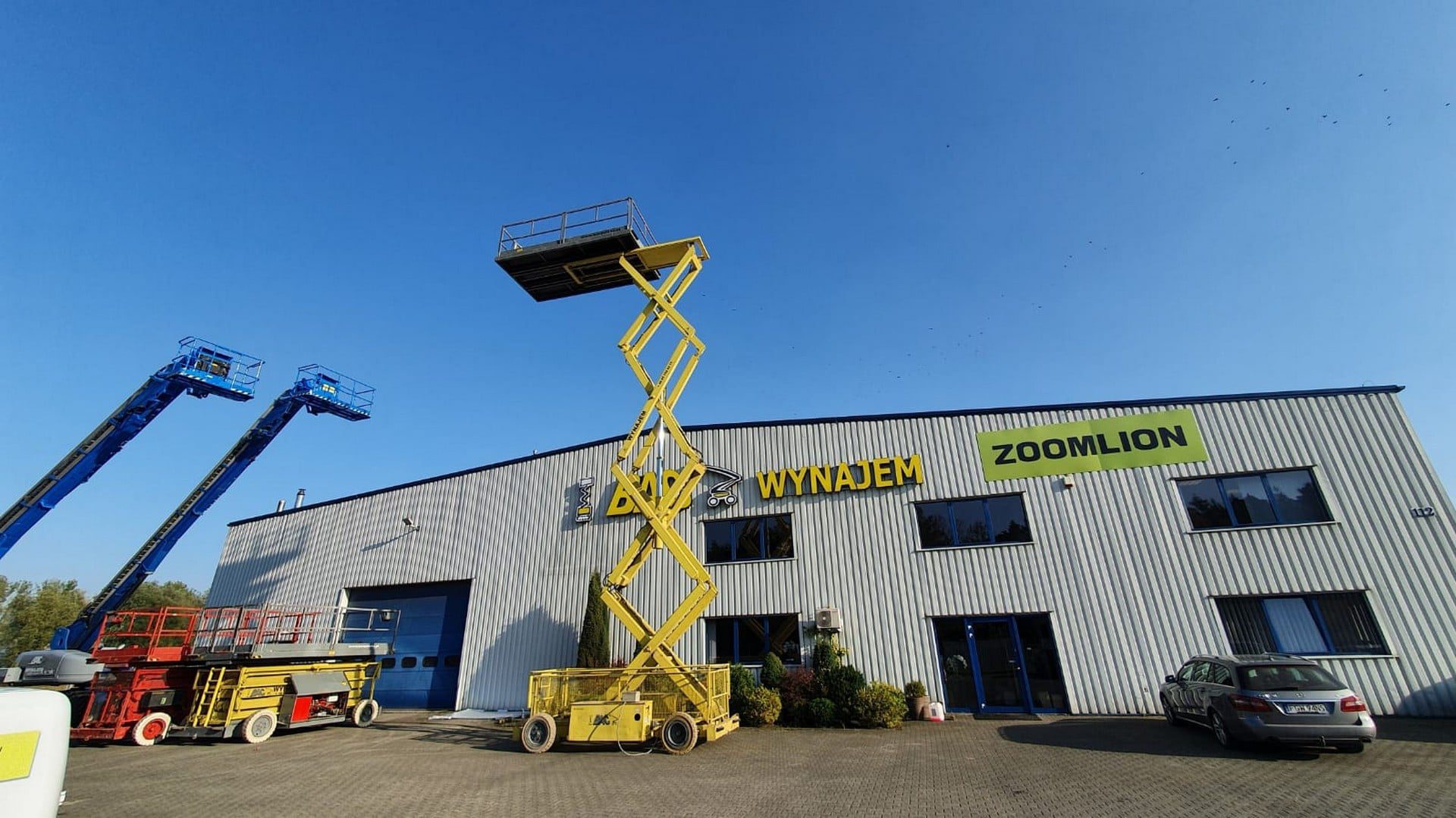 Podnośniki na terenie firmy Zoomlion, wynajem, niebieskie niebo.
