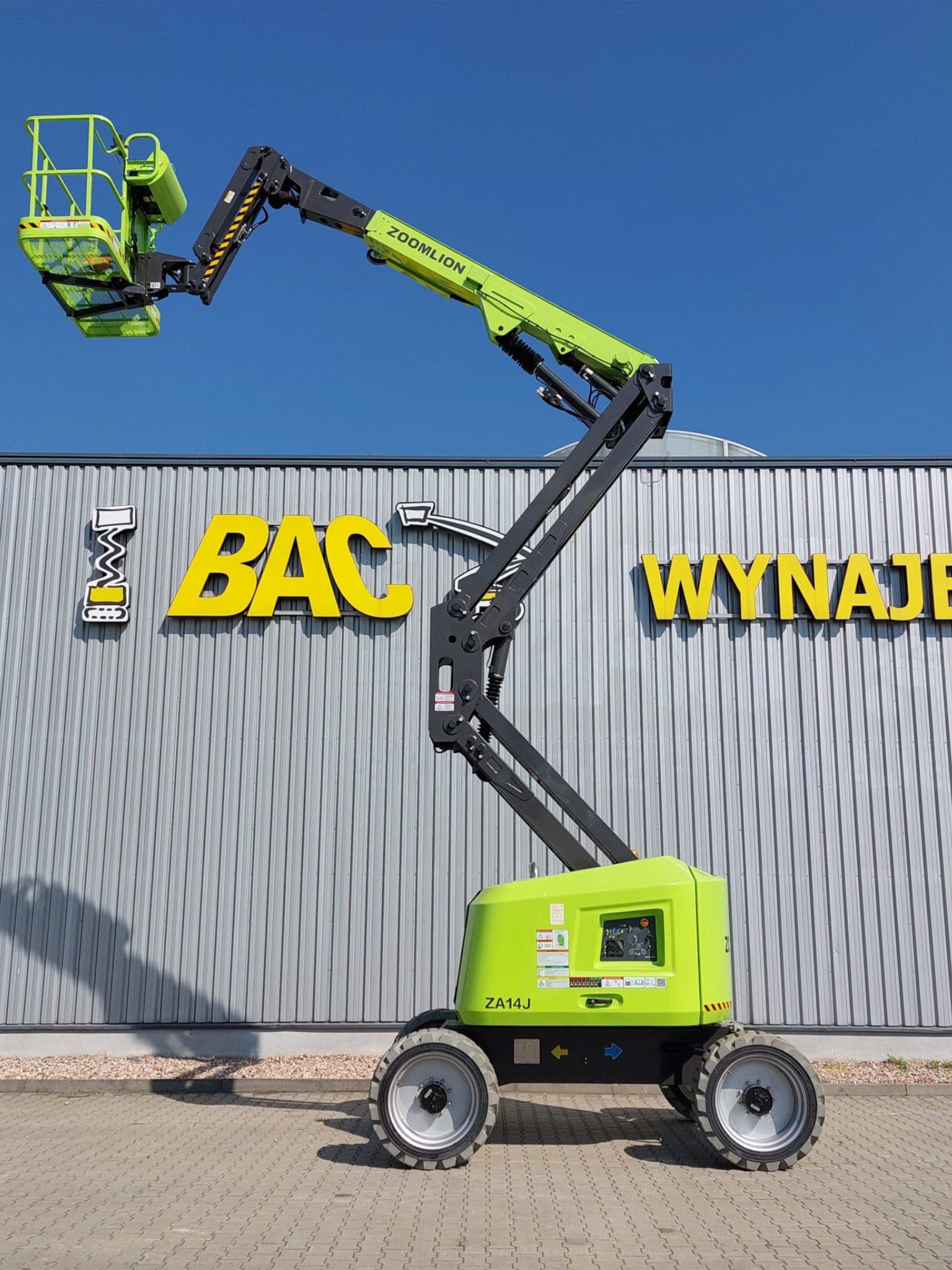 Podnośnik koszowy Zoomlion przed budynkiem z napisem Wynajem