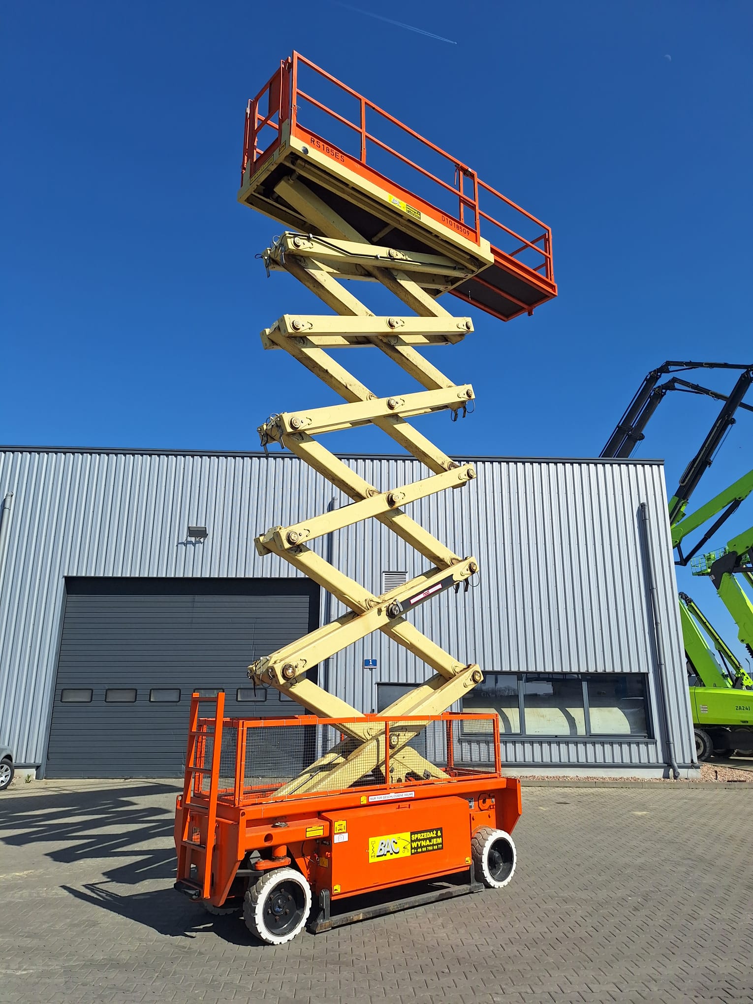 Podnośnik nożycowy Holland Lift N165EL12 – elektryczny, 16,5 m wysokości roboczej, stabilna platforma robocza, idealny do prac wewnętrznych i zewnętrznych. Wynajem w Bac Polska.