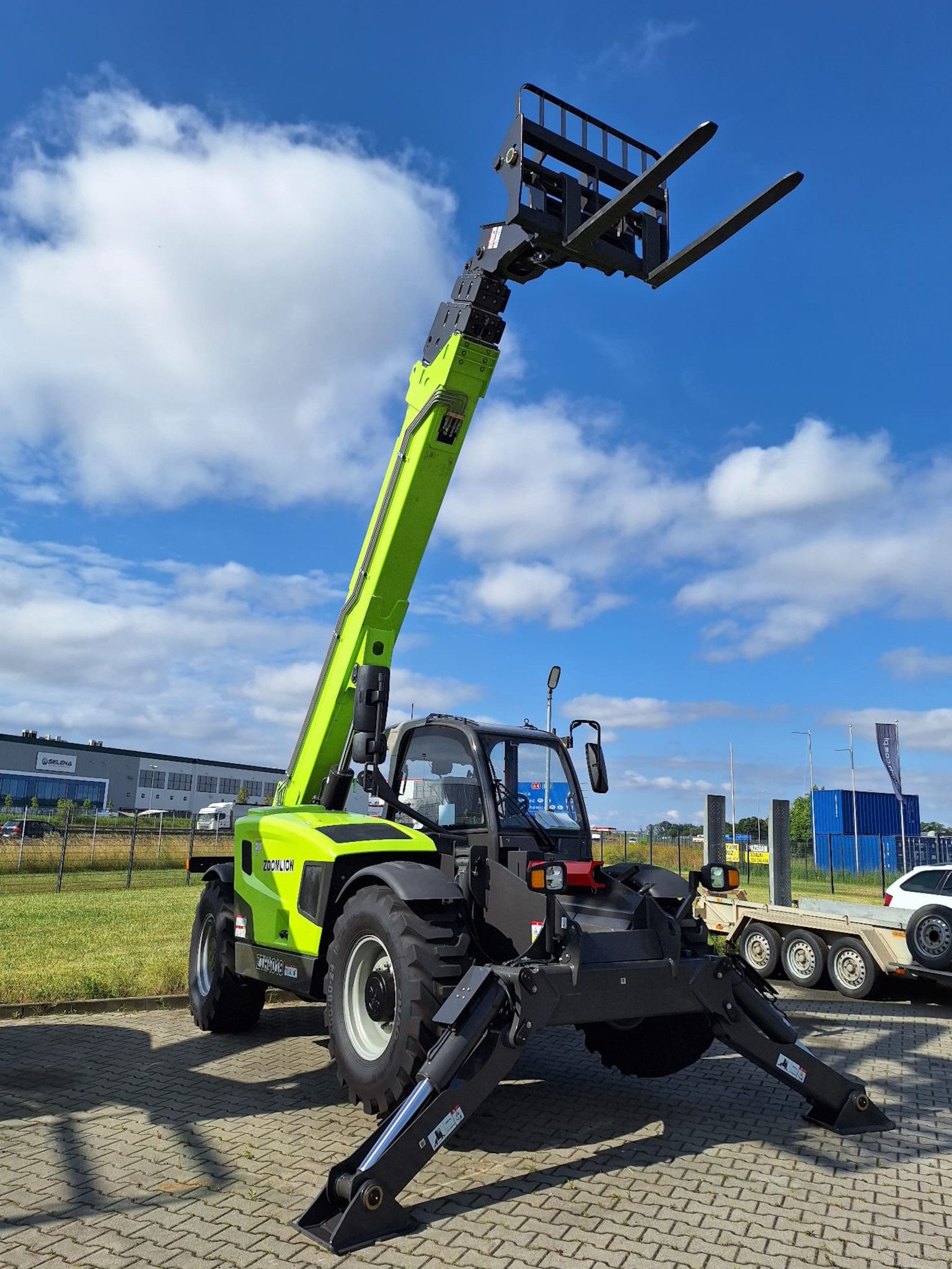 Ładowarka teleskopowa Zoomlion ZTH4018 z napędem 4x4 i dużym prześwitem, widok z boku w trakcie pracy na placu budowy – ramię uniesione, kabina klimatyzowana.