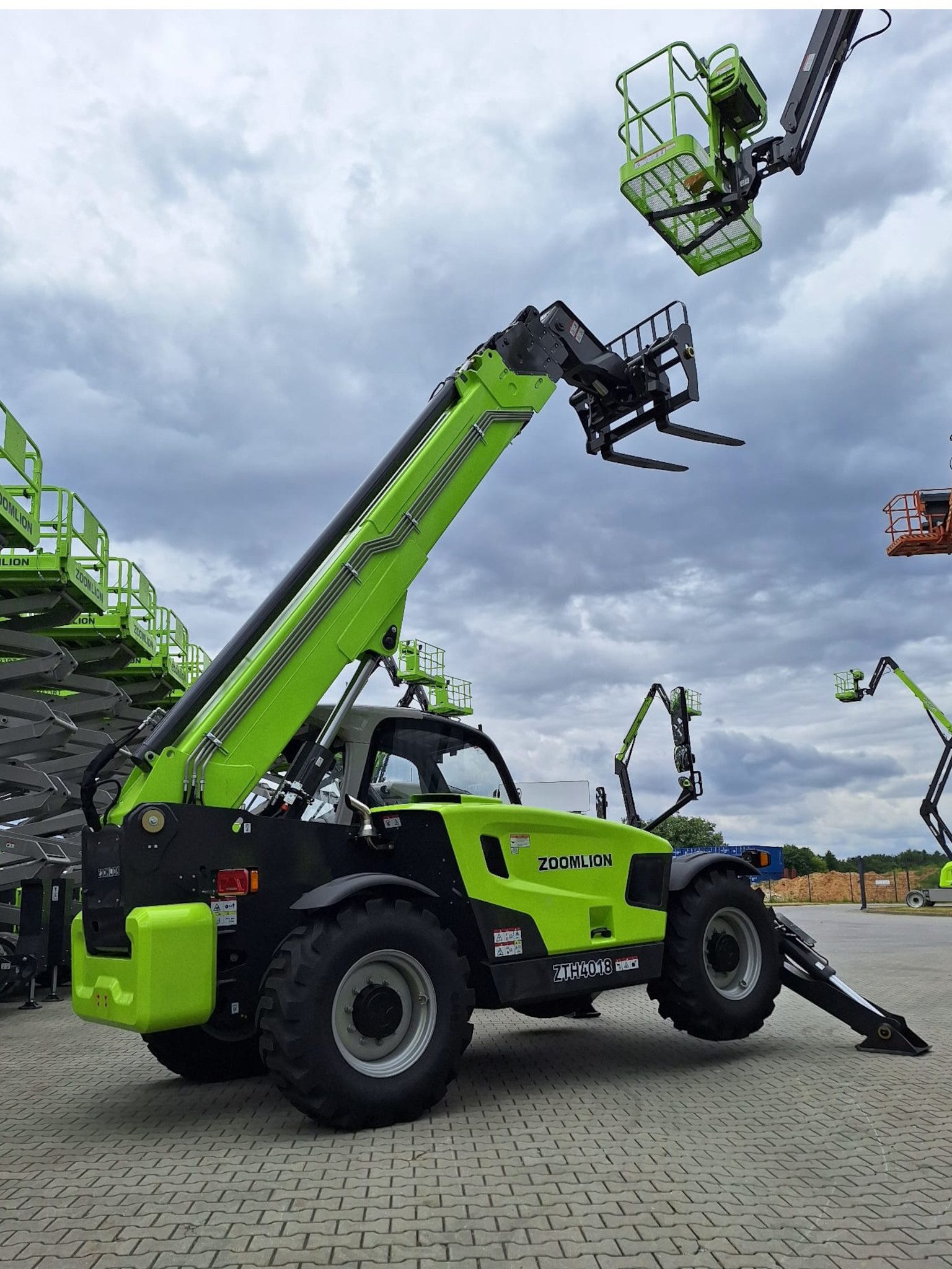„Ładowarka teleskopowa Zoomlion ZTH4018 z napędem 4x4 i dużym prześwitem, widok z boku w trakcie pracy na placu budowy – ramię uniesione, kabina klimatyzowana.