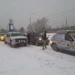 Rally cars in a winter landscape near a gas station.