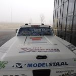 A van with an advertisement in front of a building on a foggy day.