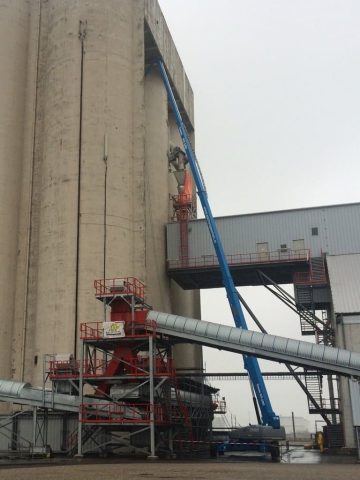 Przemysłowy silos z podnośnikiem koszowym i rurami.