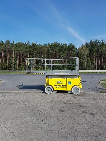 Scissor lift by the roadside in a forested setting.