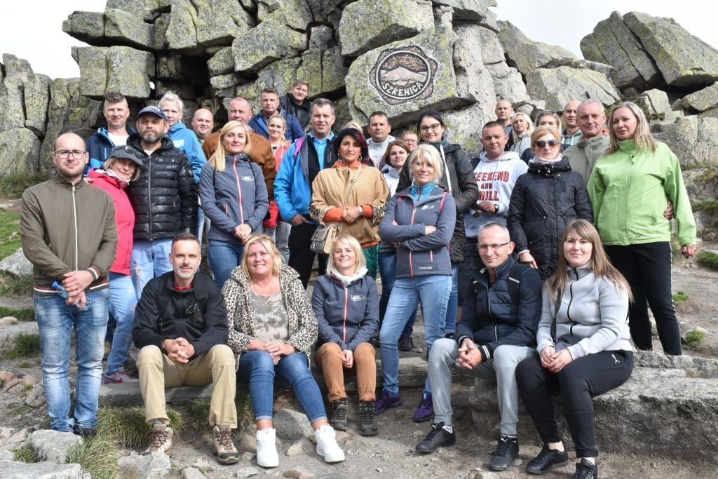 A group of people in front of a rock monument in the mountains.