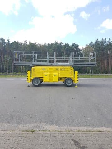 Yellow scissor lift next to the road.