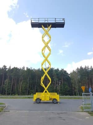 Scherenhebebühne auf dem Parkplatz vor dem Wald.