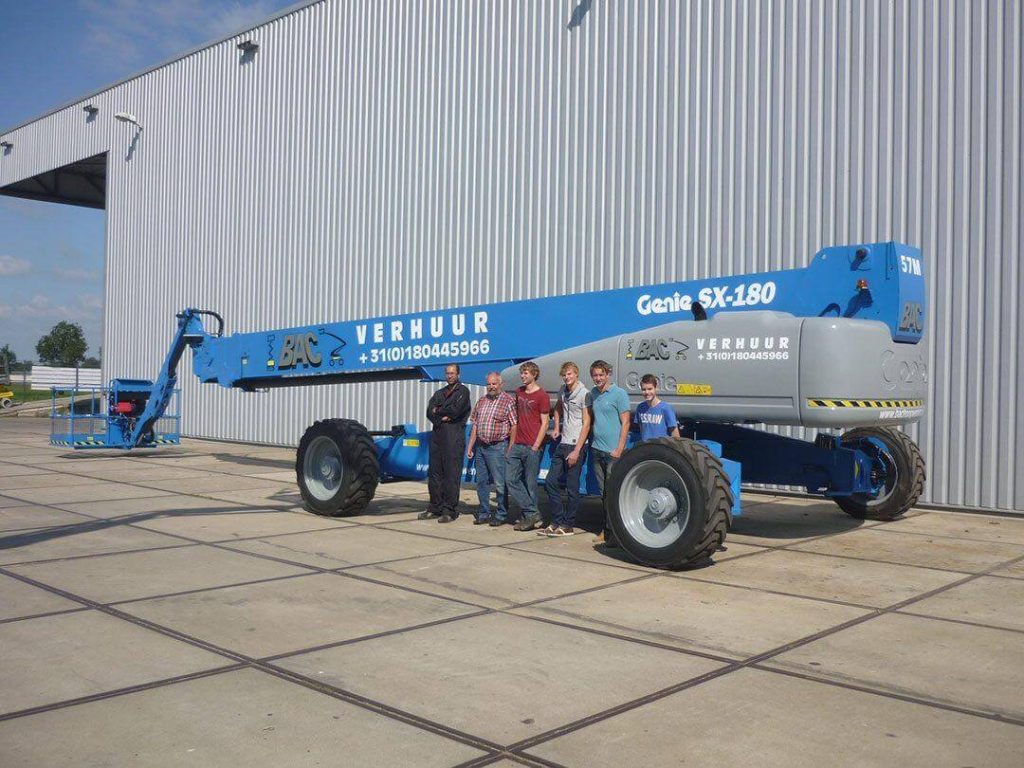 A group of people next to a Genie SX-180 telescopic elevator