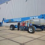 A group of people next to a Genie SX-180 telescopic elevator