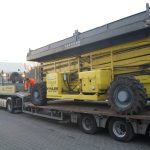 Ein Lastwagen, der einen gelben Kran auf einem Anhänger transportiert.
