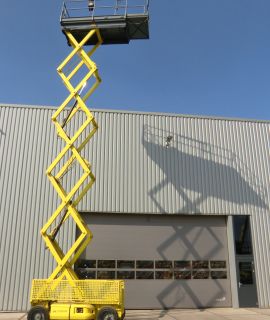 Yellow scissor lift in front of an industrial building.