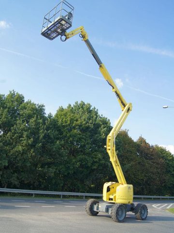 A basket lift on a construction site next to trees.