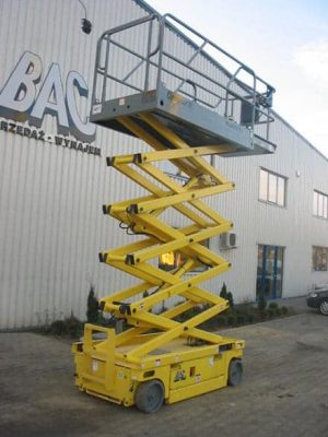 Yellow scissor lift in front of an industrial building.