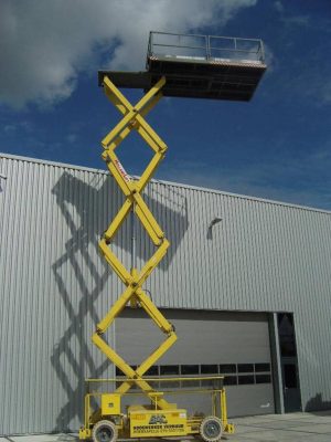 Yellow scissor lift in front of an industrial building.