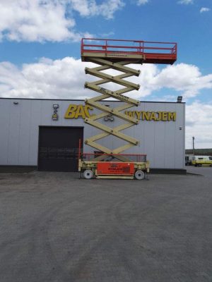 A scissor lift in front of a building with a sign reading "Rental."