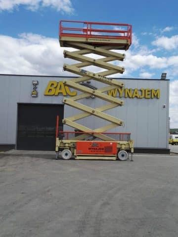 A scissor lift in front of a building with a sign reading "Rental."