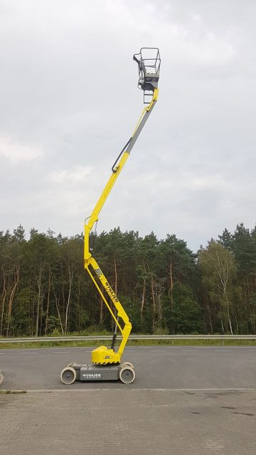 Podnośnik teleskopowy żółty na zewnątrz przy drodze.