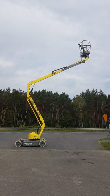 Podnośnik koszowy na drodze obok lasu