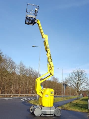 Podnośnik koszowy na drodze obok lasu.