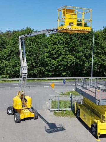 Yellow scissor lift outside by the trees.