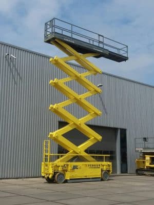 Yellow scissor lift in front of an industrial building.