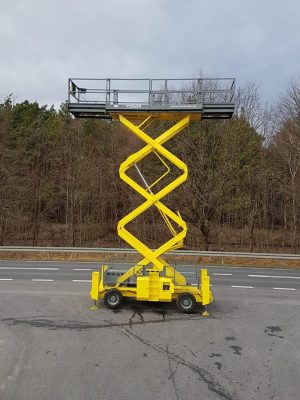 Yellow scissor lift on the road next to the forest