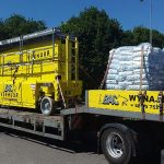 A truck carrying yellow construction equipment and pallets.