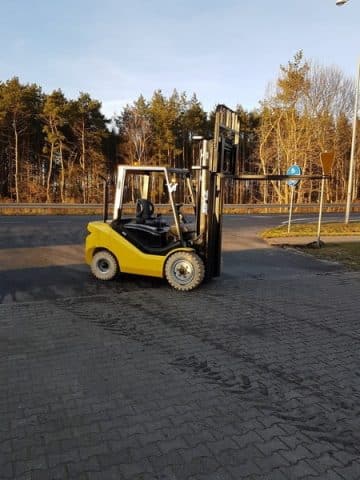 A yellow forklift on an asphalt parking lot.