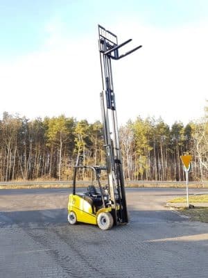 Żółty wózek widłowy z wysokim masztem na parkingu.