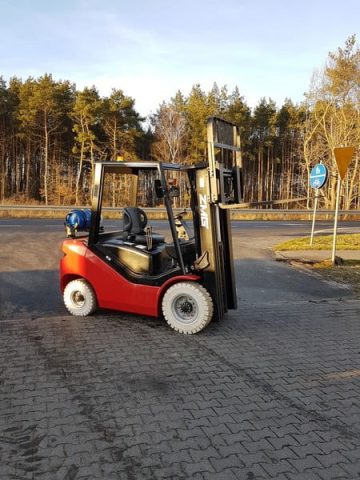 A red forklift on an asphalt parking lot.