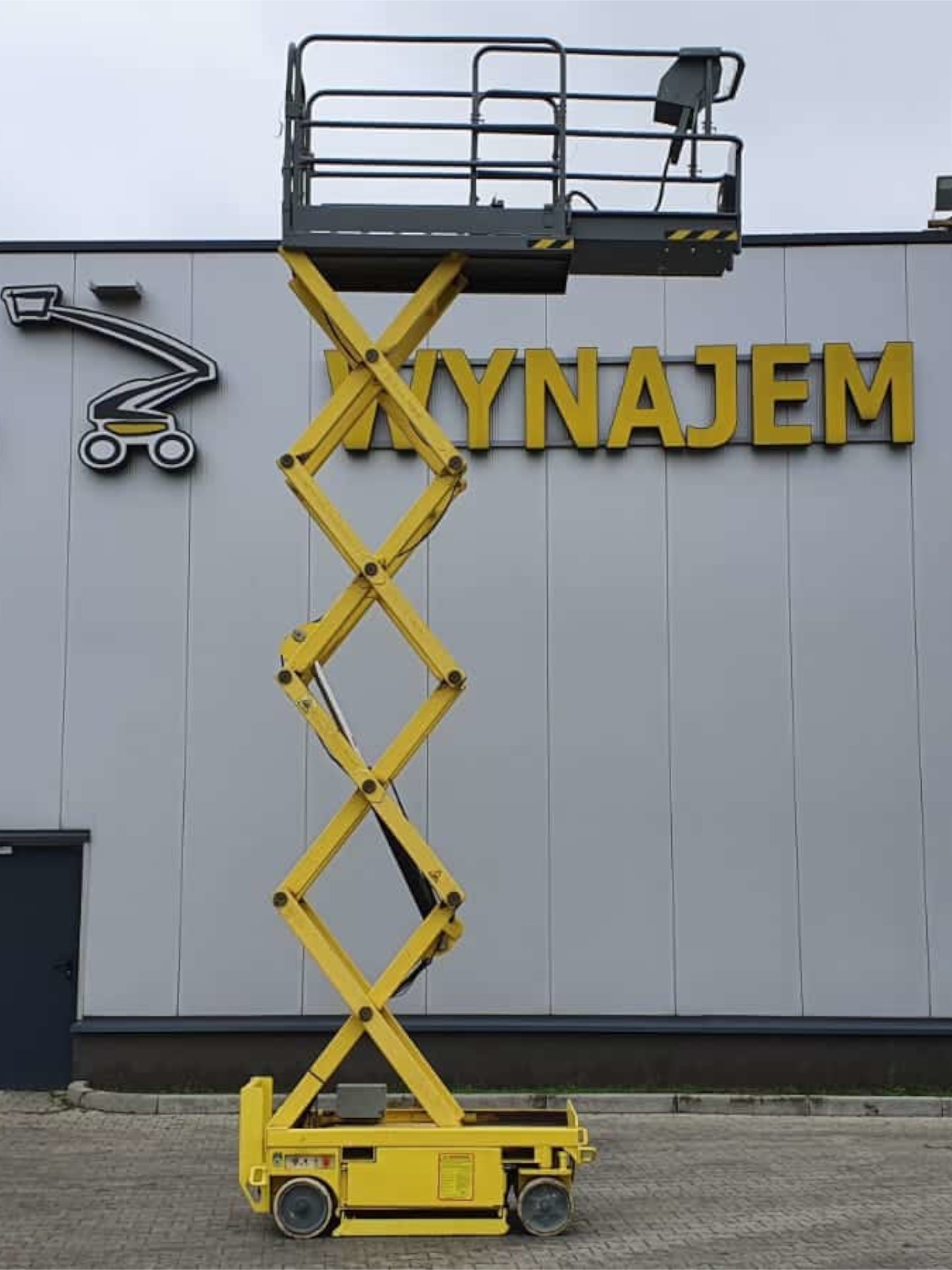 Żółta podnośnikowa platforma przed halą z napisem BAC WYNAJEM