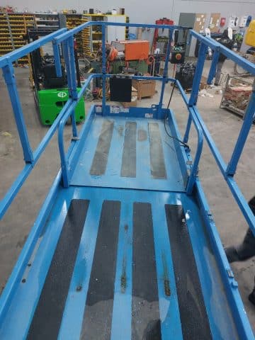 Scissor lift in a warehouse with an employee.