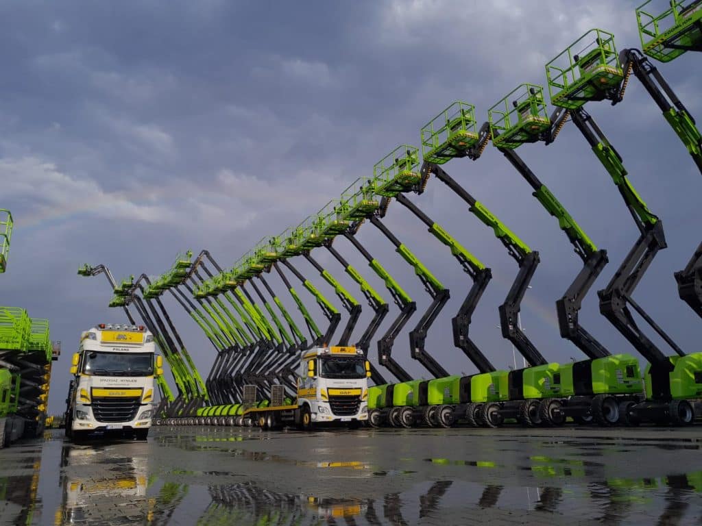 Aerial work platforms and trucks on wet asphalt.